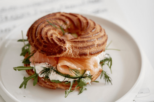The photo shows a bagel topped with salmon and cream cheese, garnished with rocket and dill.